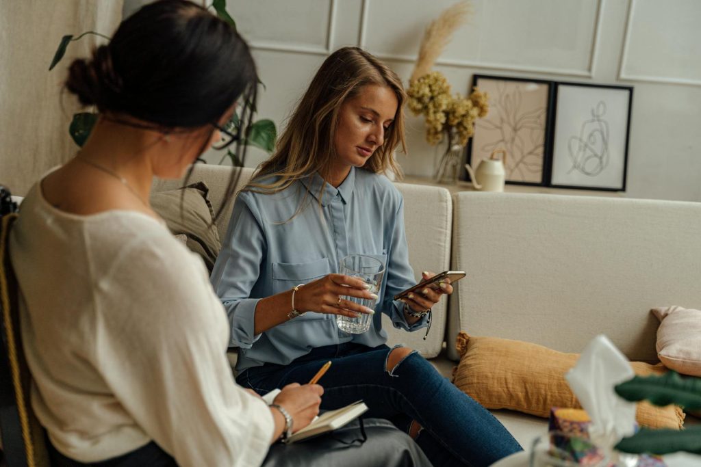 Woman in Blue Denim Jacket Sitting Beside Woman in White Shirt